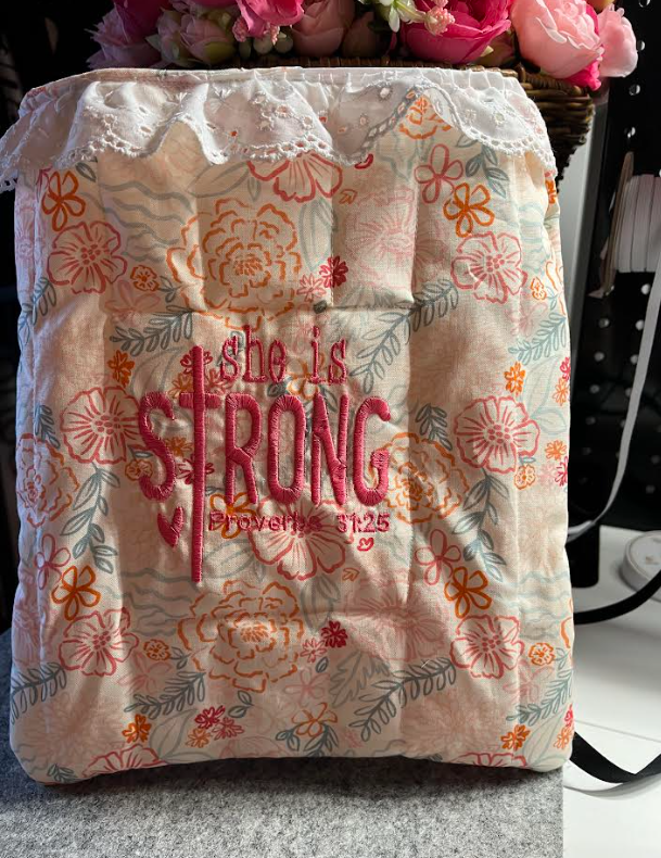Floral-patterned bag with 'She is Strong' text on a blurred background